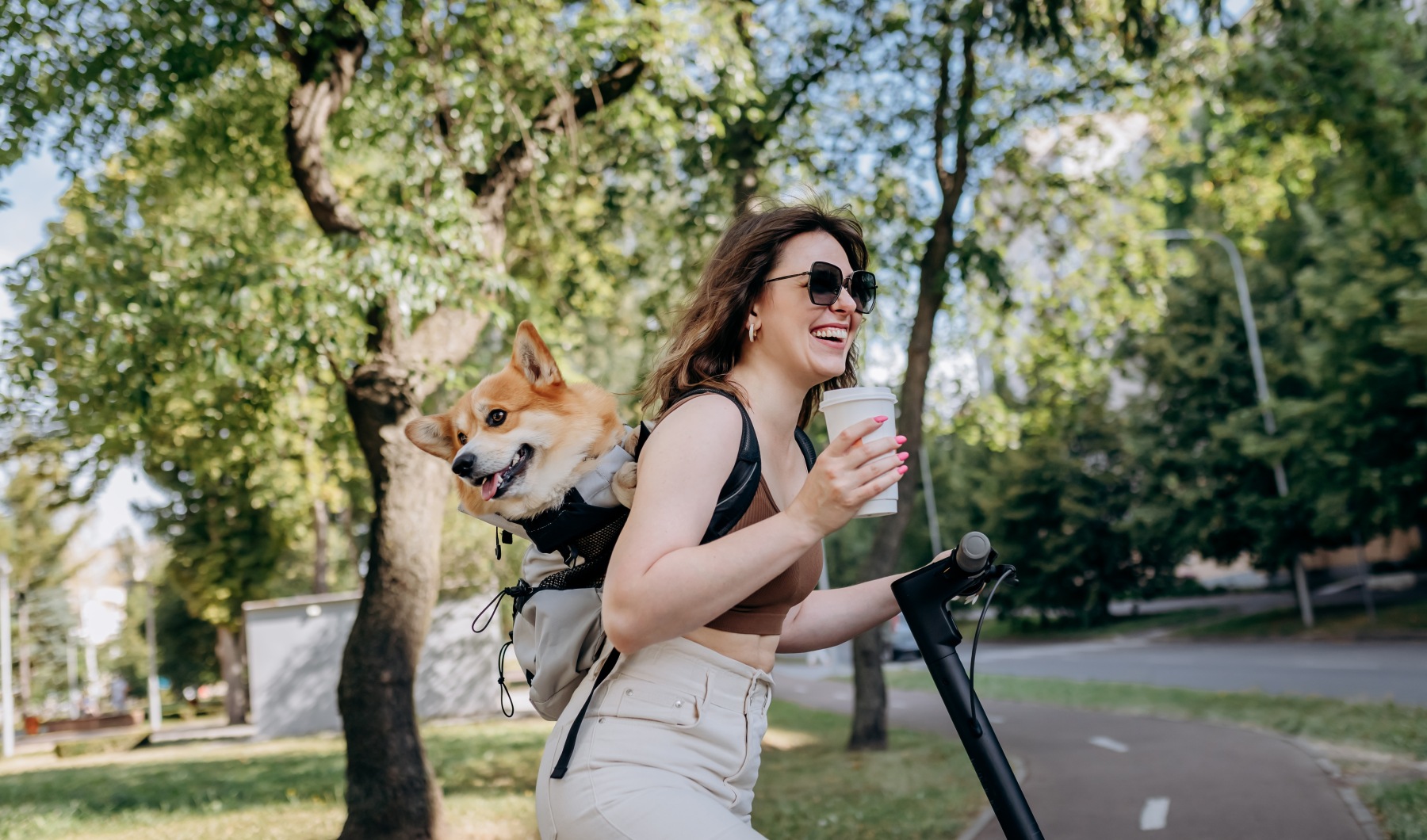 Girl with a corgi on her back riding a scooter